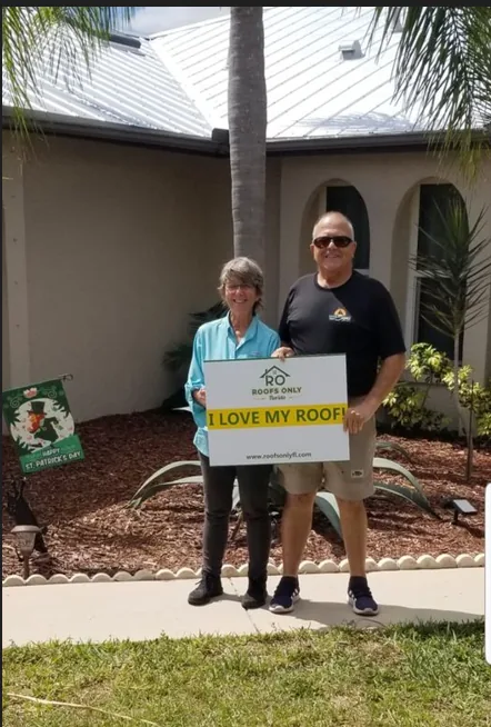 Two homeowners holding an I Love My Roof sign outside their home