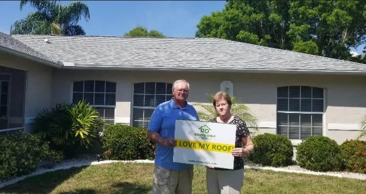 Two homeowners holding an I Love My Roof sign in front of their home